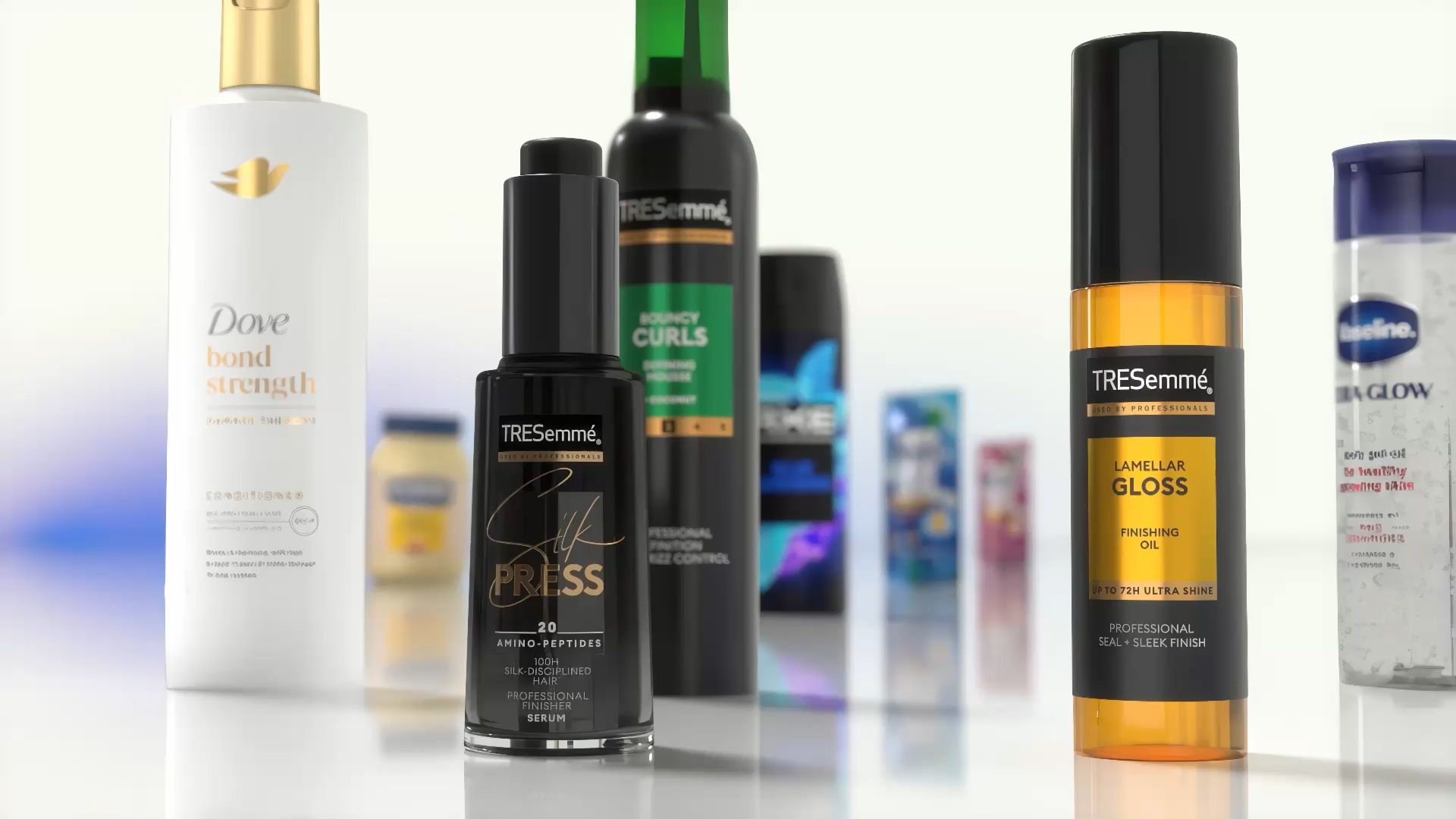 Gros plan sur divers produits de soins capillaires et corporels présentés sur une surface réfléchissante. On distingue notamment l'après-shampoing Dove Bond Strength, le sérum TRESemmé Silk Press, l'huile de finition TRESemmé Lamellar Gloss et d'autres produits Unilever en arrière-plan.